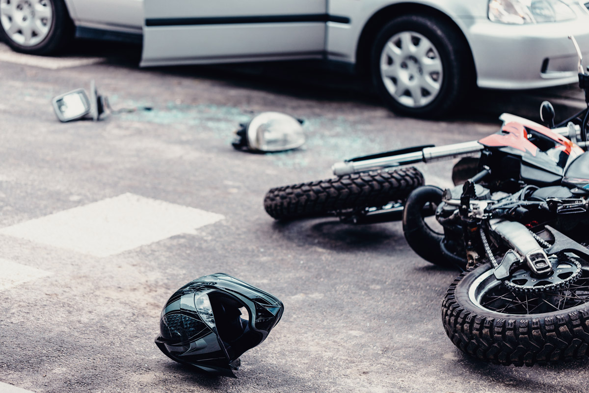 Helmet and motorcycle next to broken peaces of a car on the street after car crash. OlsenDaines serving Oregon and Washington talk about what to do if you're a passenger in a motorcycle accident.