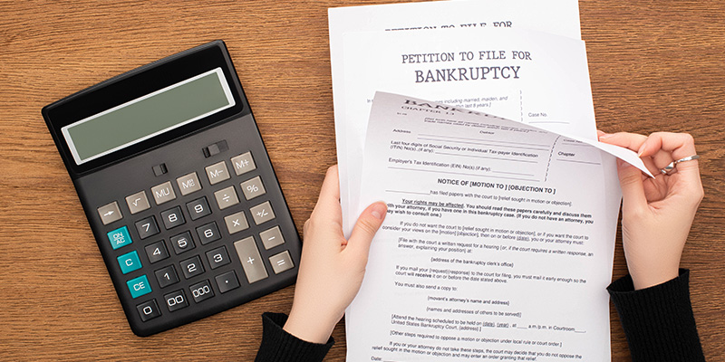 cropped view of woman with Chapter 7 bankruptcy papers near calculator on wooden background