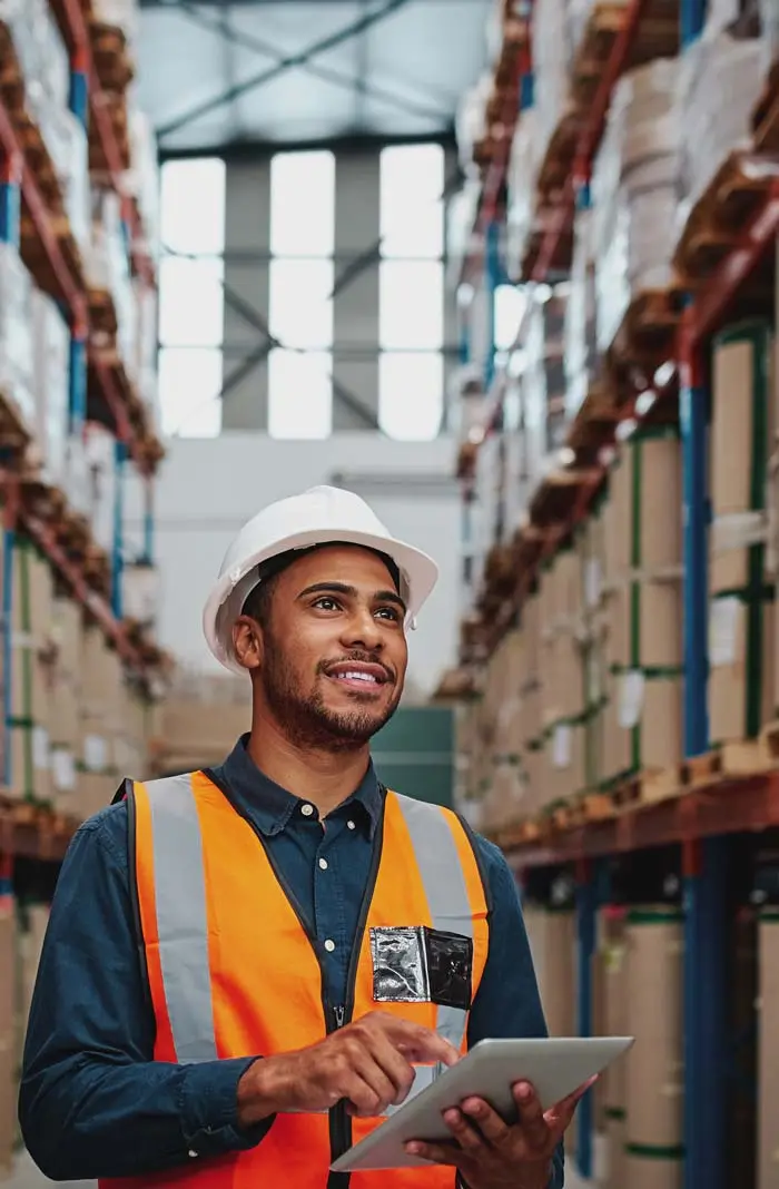 Man in orange vest and hardhat holds tablet in a busy warehouse. OlsenDaines is one of the top personal injury law firms in Oregon and Washington.