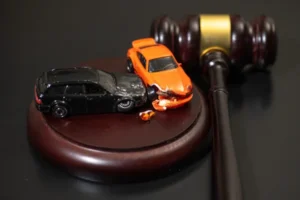 Two toy cars depicting a vehicle crash resting on a judge's wooden block next to a legal gavel.