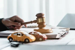 Auto attorney holding a wooden gavel over legal documents alongside miniature toy cars representing an auto accident claim.