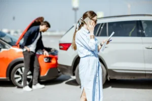 A woman making a phone call while holding documents after a rear-end car accident.
